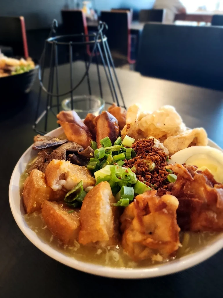 Close-up of a richly garnished savory noodle soup in a white bowl.