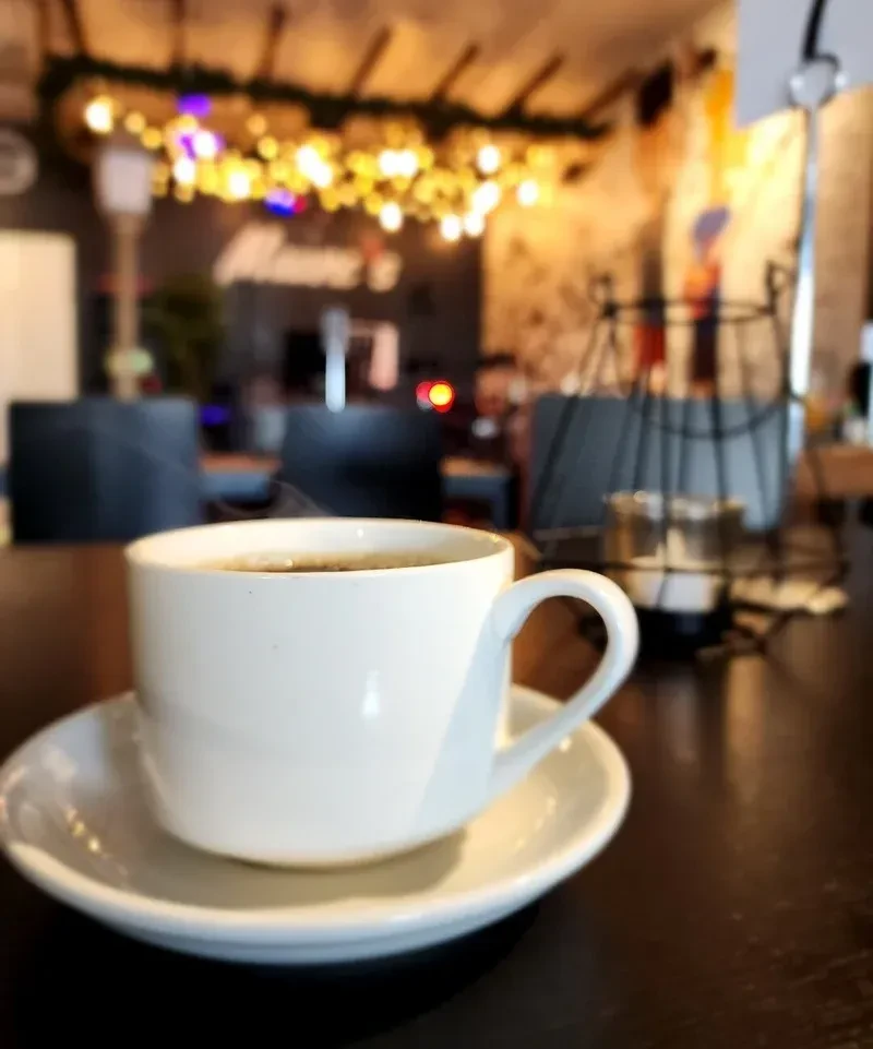 White ceramic coffee cup with steam in a blurred cafe.