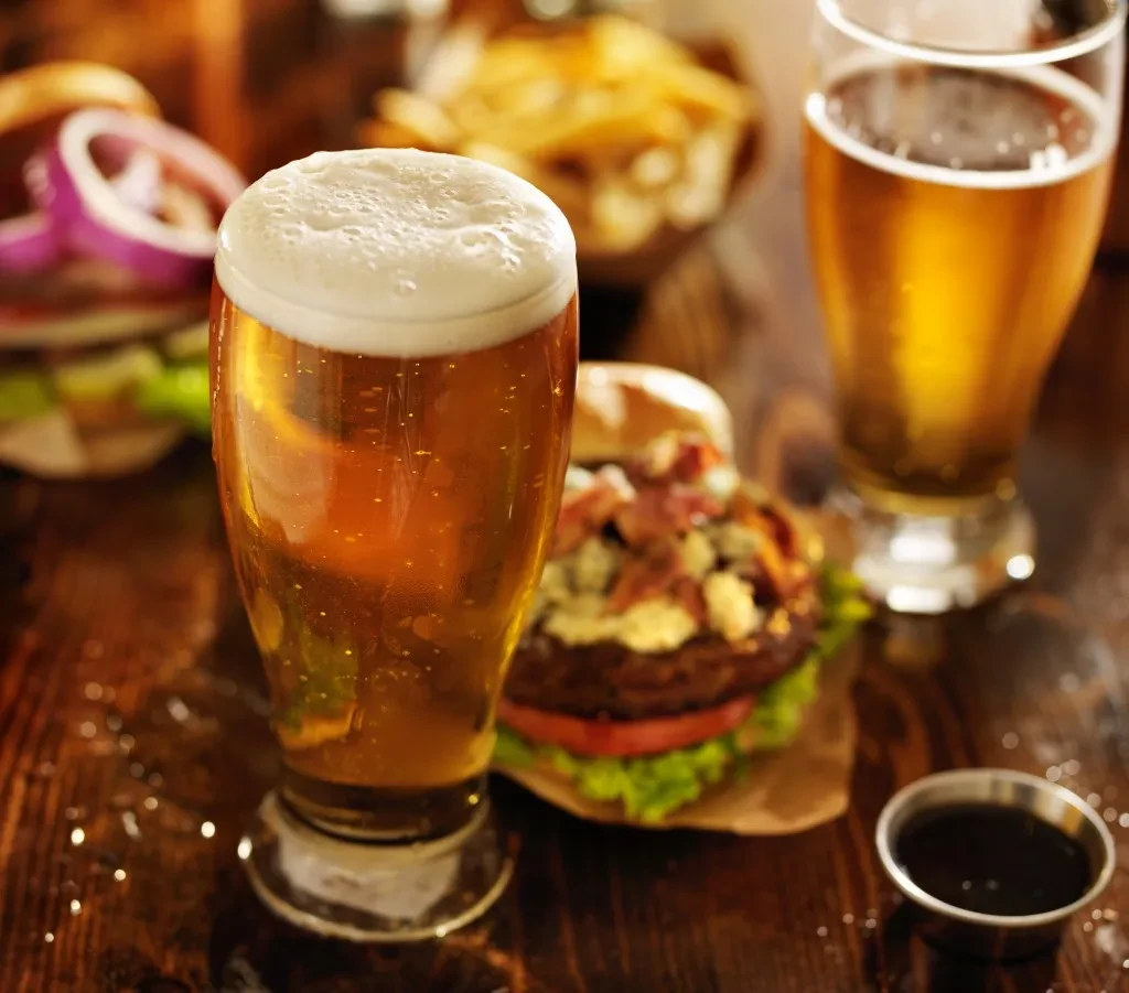 Frothy amber beer, condensation, gourmet burger, and fries.