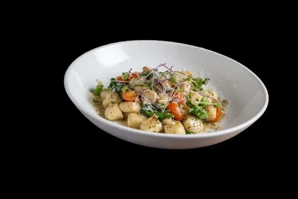 Golden gnocchi with tomatoes, leafy greens, and cheese in a white bowl.