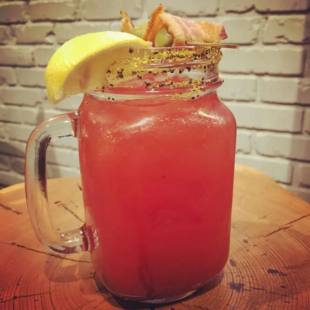 Mason jar Bloody Mary with lemon, spiced rim, olives, and bacon.