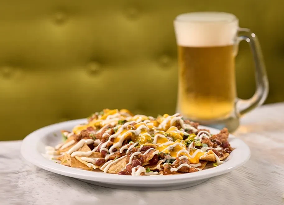 Loaded nachos with cheese, meat, and beans, beer in background.