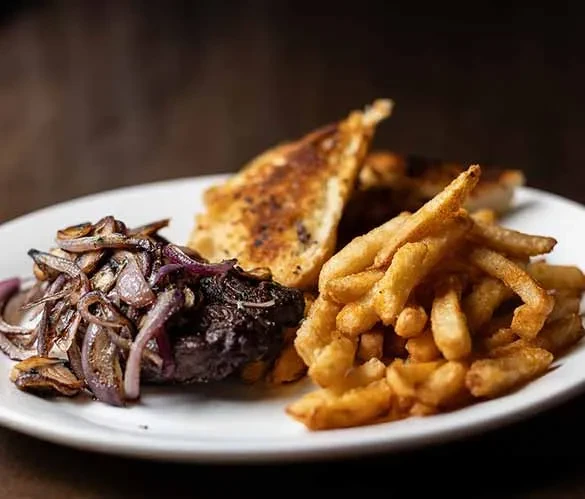 A plate of meat, caramelized onions, mushrooms, bread, and golden fries.