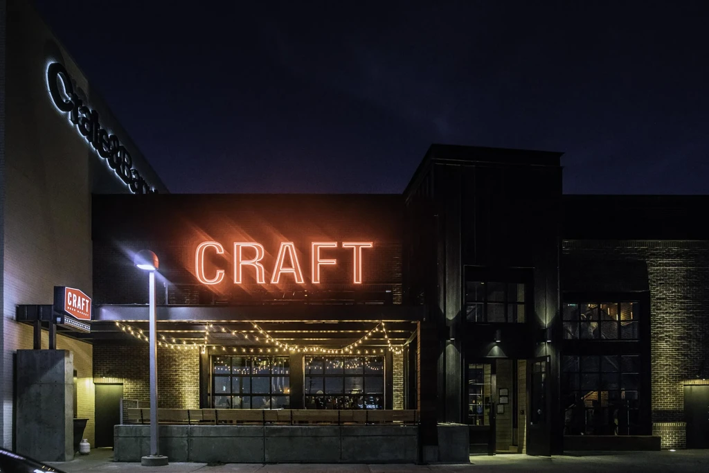 Modern 'CRAFT' restaurant, bright orange neon, and lit patio at night.