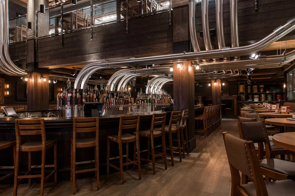 Spacious, upscale industrial bar with numerous beer taps and dark wood.