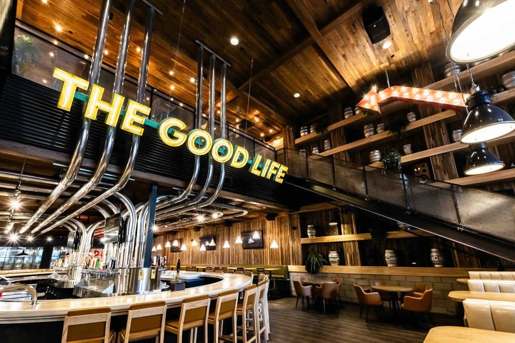 Rustic-industrial bar interior with beer taps and "THE GOOD LIFE" neon sign.