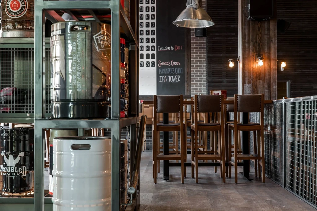 Industrial-style brewery interior with beer kegs, bar stools, and chalkboard menu.
