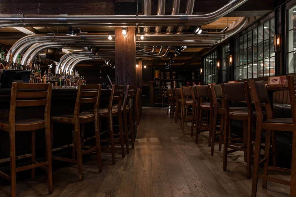 Rustic-industrial bar and restaurant with dark wood, metal, and warm lighting.
