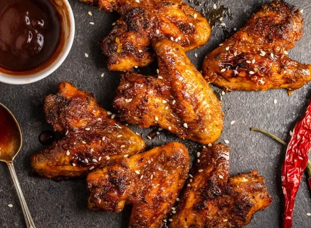 Glossy, sesame chicken wings with dark dipping sauce and red chili peppers.
