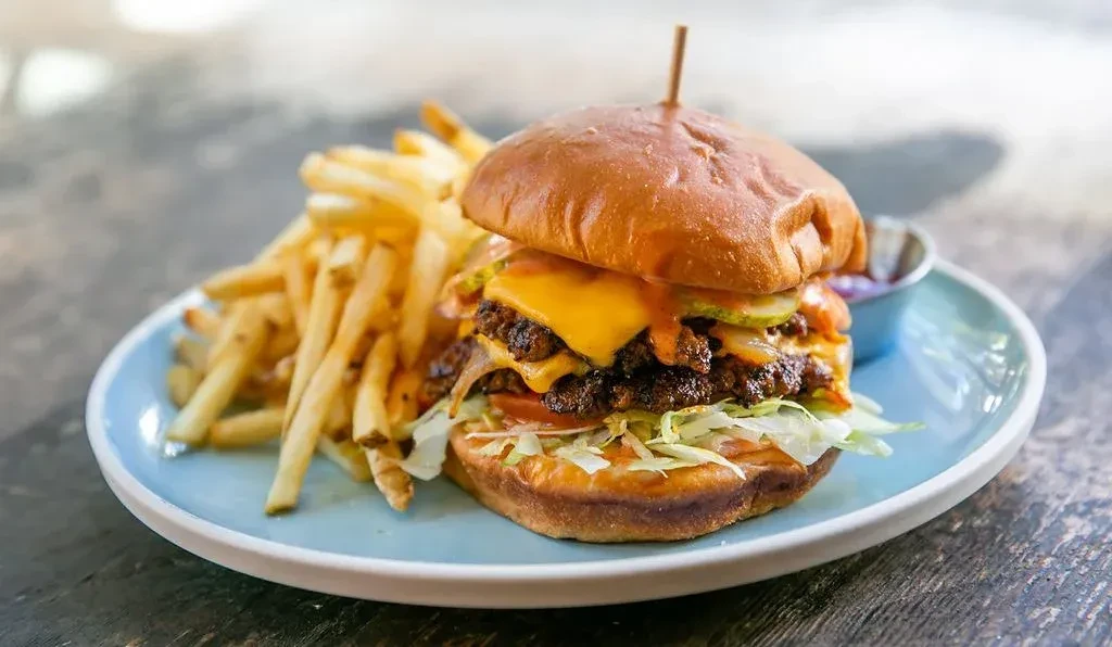 Stacked double cheeseburger and golden french fries on a blue plate.