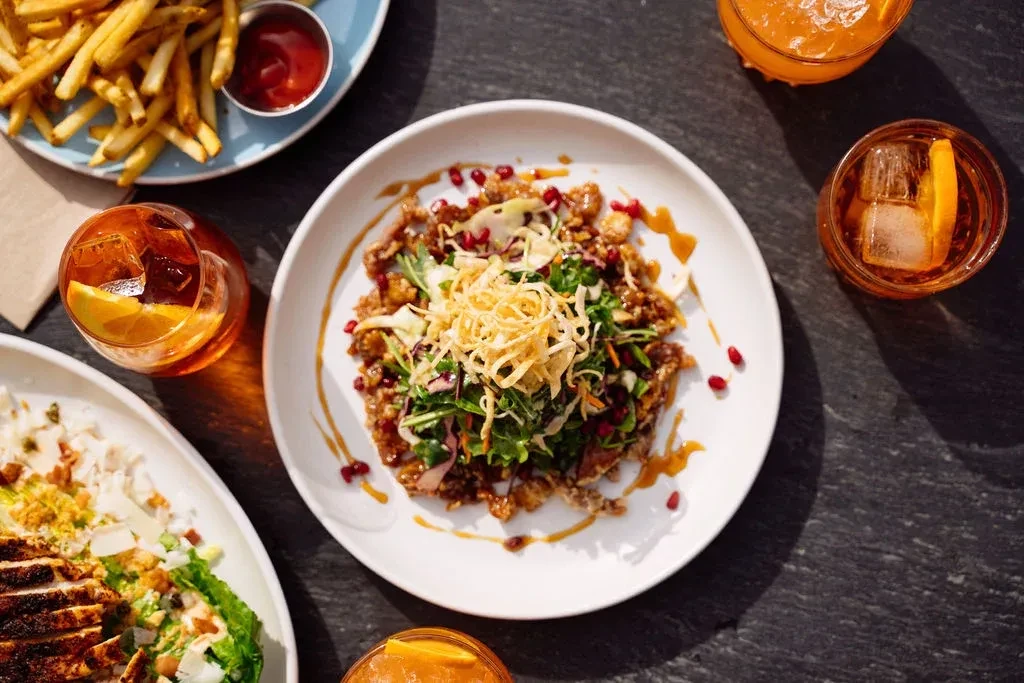 Overhead: Fried chicken, fries, salads, and cocktails on a dark table.