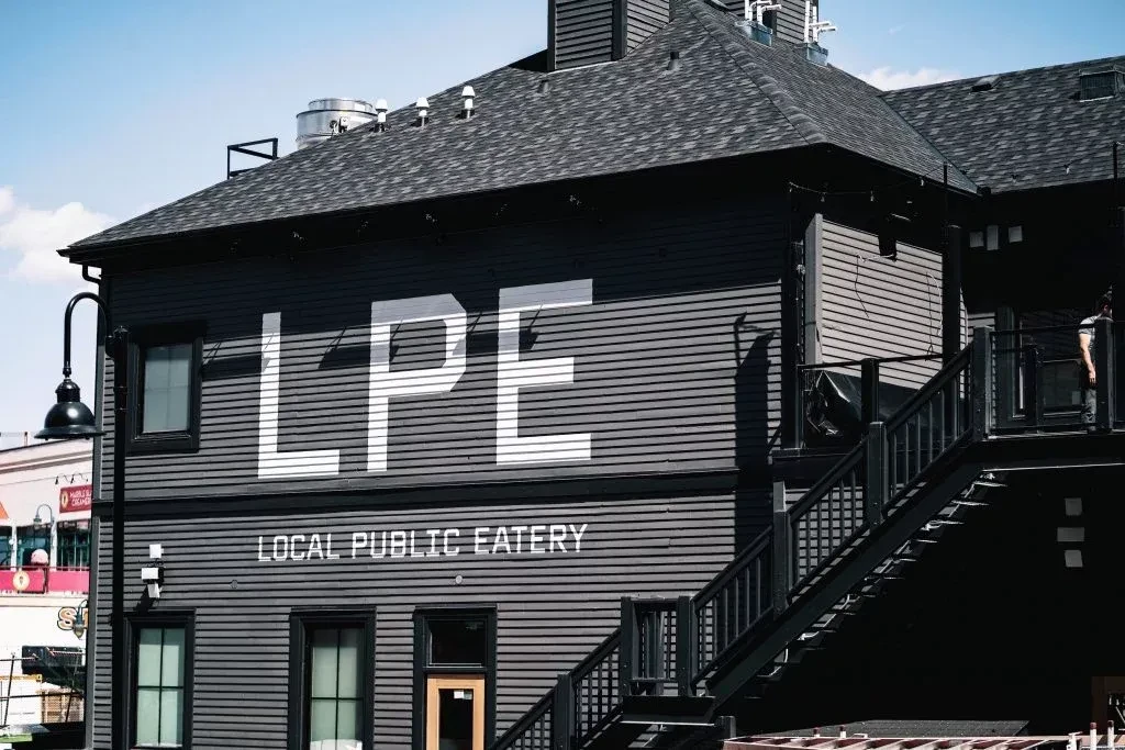 Dark gray "LPE LOCAL PUBLIC EATERY" building, modern stairs to patio.