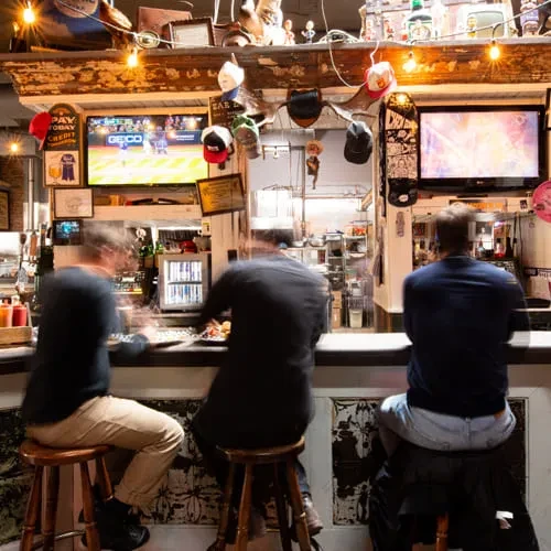 Blurred people in a warm, rustic bar with TVs and food.
