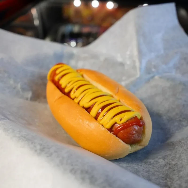 A single hot dog with mustard and ketchup on crumpled deli paper.