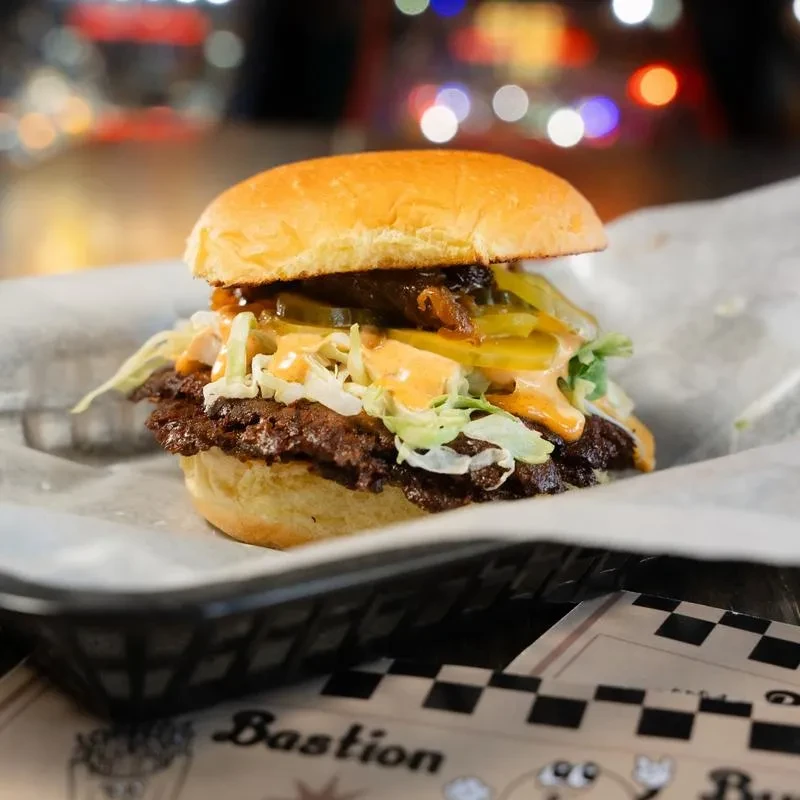 High-stacked burger with two patties in basket on branded mat.