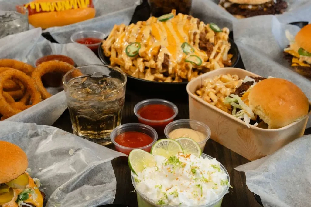 Diverse fast-food meal with burgers, fries, onion rings, hot dog, and dessert.