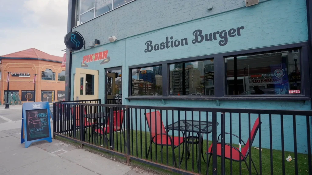 Light blue building housing Bastion Burger and Pin Bar, with an outdoor patio.