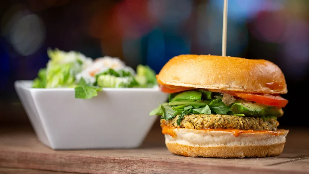 Close-up of a vegetarian burger with avocado and salad on a wooden surface.