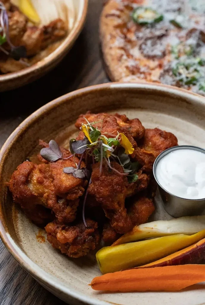 Deep-fried chicken pieces with reddish sauce, microgreens, carrots, and white dip.