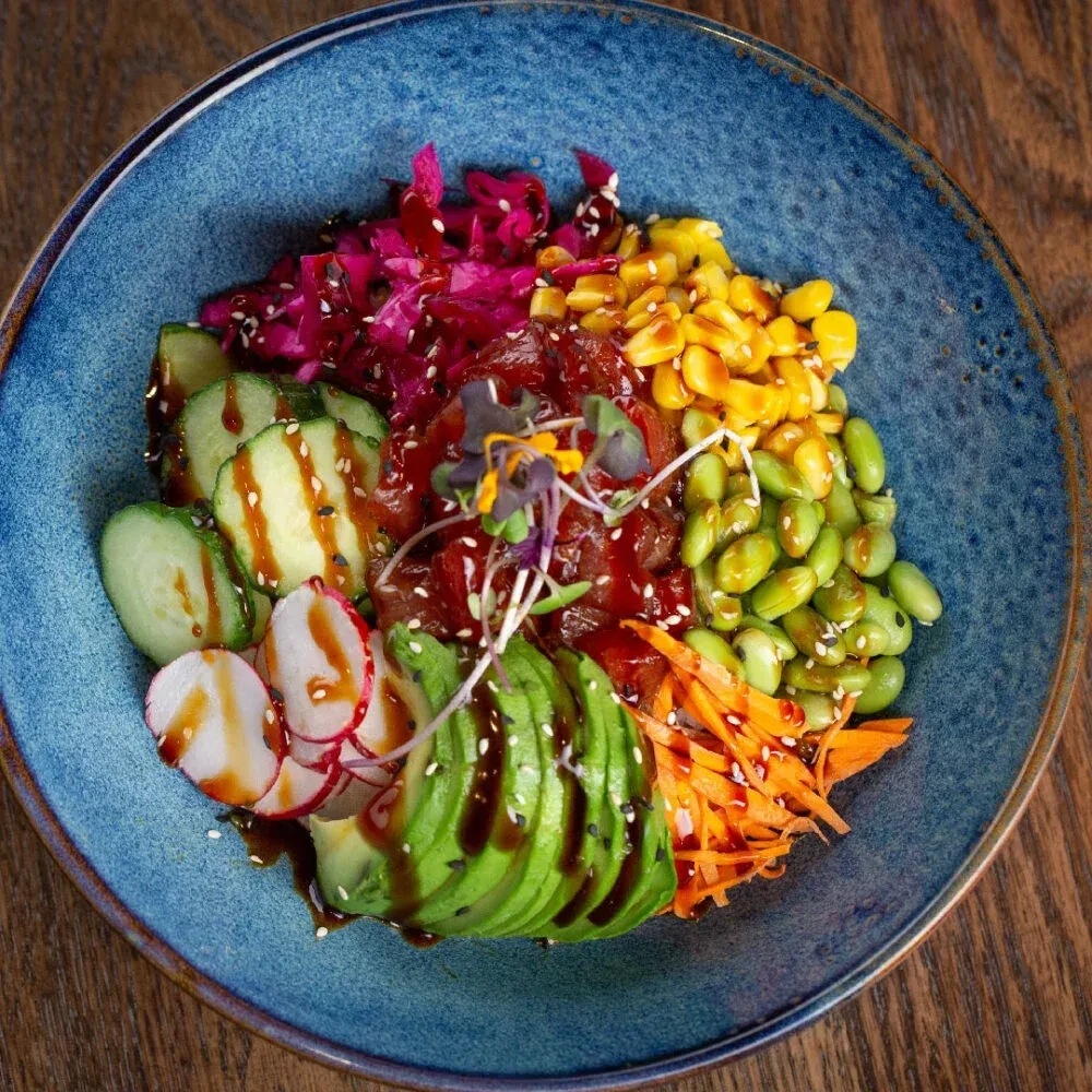 Colorful poke bowl with fish, vegetables, and sauce in a blue bowl.