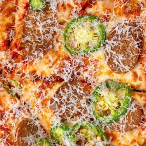 Top-down pizza with melted cheese, green jalapeños, and sausage.