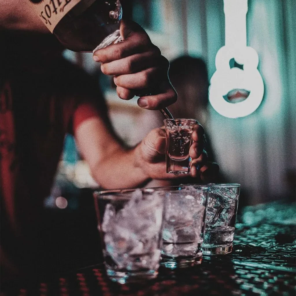 Hands pour Tito's into a shot glass at a dim bar.