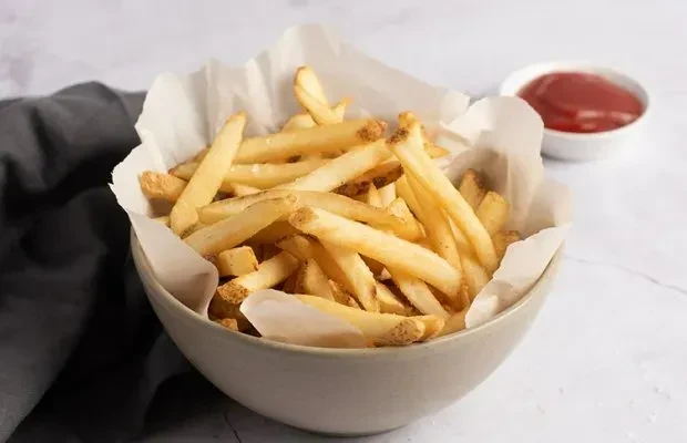 Ceramic bowl of crispy golden-brown french fries and ketchup.