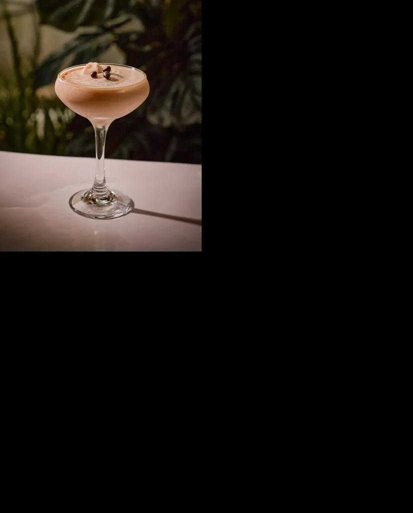 Creamy beige drink in coupe glass, whipped topping, dark garnish, green background.
