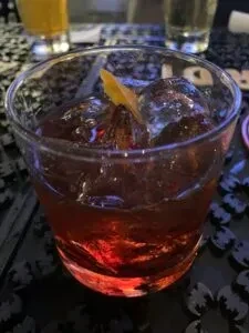 Dark red cocktail, glowing, with ice and orange peel, bat decor.