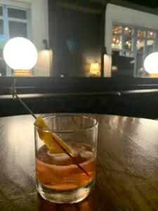 Amber cocktail in rocks glass with ice and citrus twist.