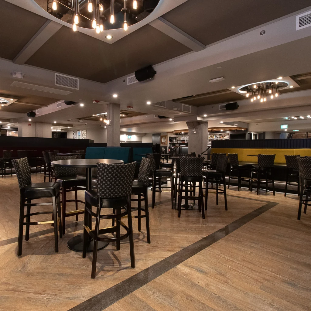 Modern restaurant interior featuring colorful booths, high-top tables, and a bar.