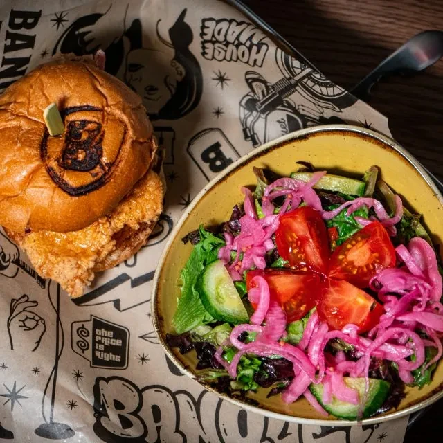 Top-down: Branded chicken burger, vibrant salad, on custom paper.