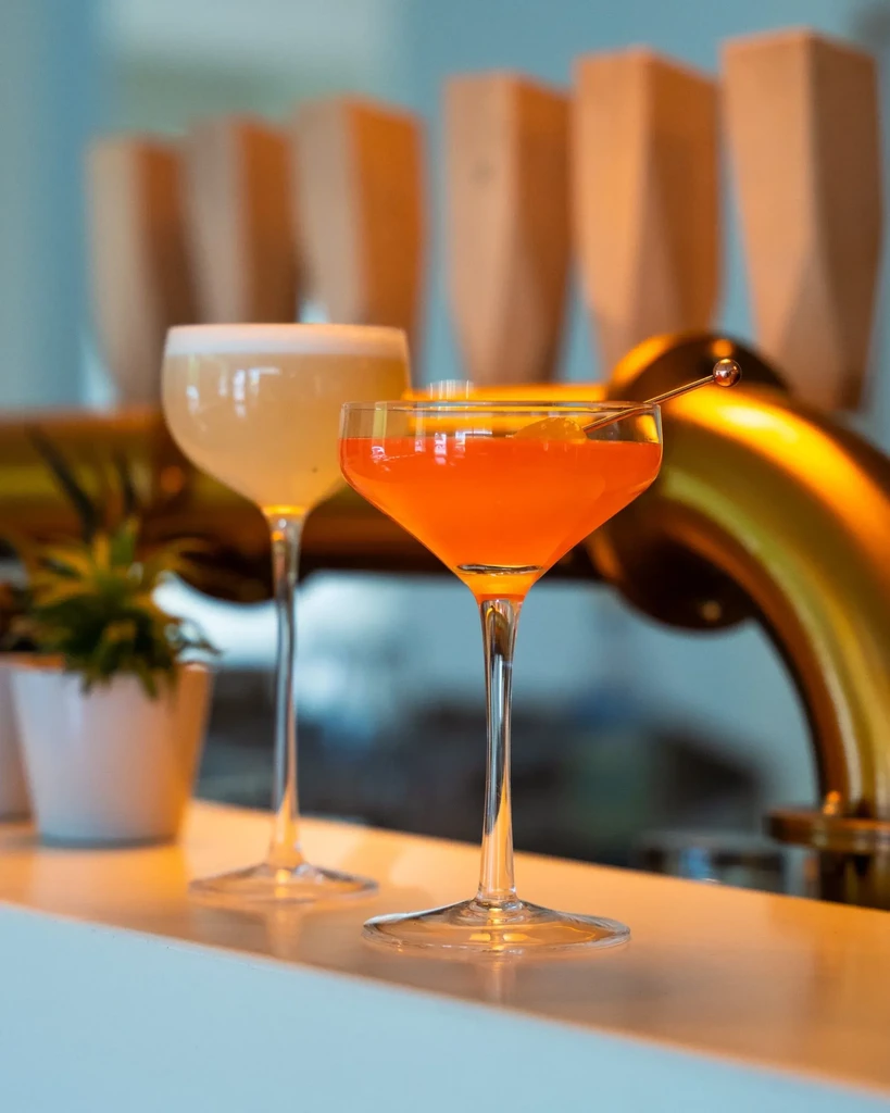 Vibrant orange and frothy yellow cocktails are elegantly displayed on a bar.