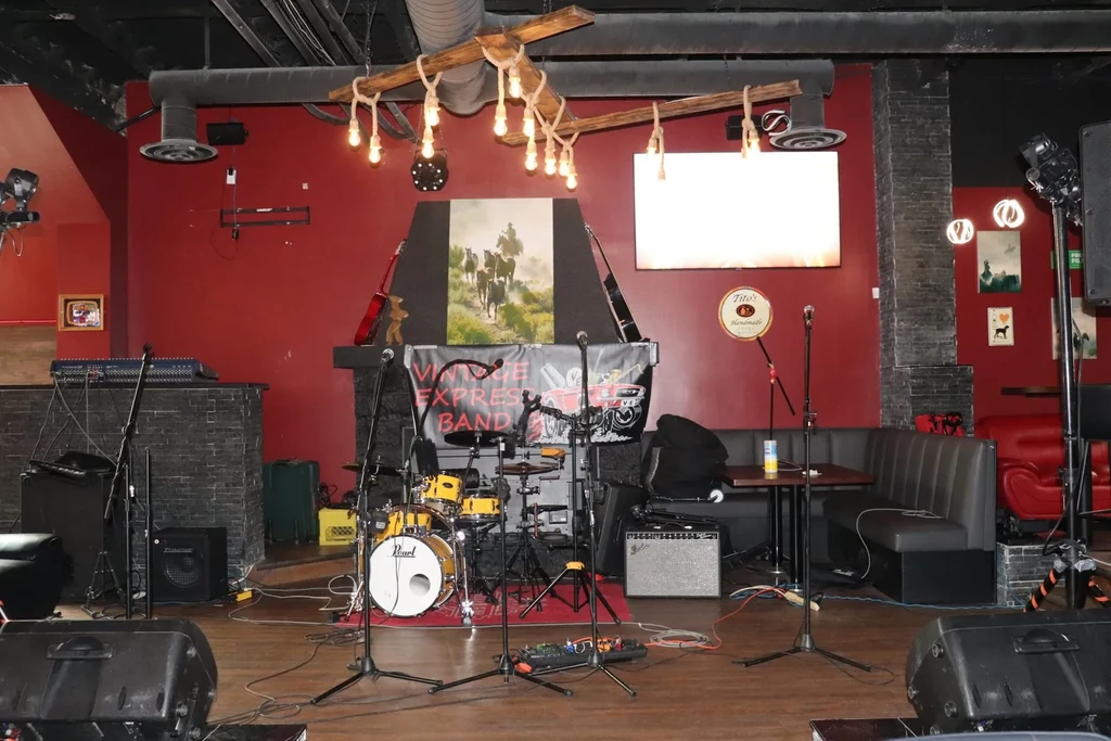 Empty live music stage with drum kit, amplifiers, and band banner.