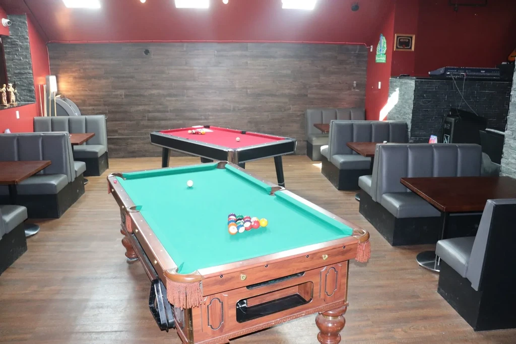 Casual bar interior featuring two pool tables, booth seating, and red walls.