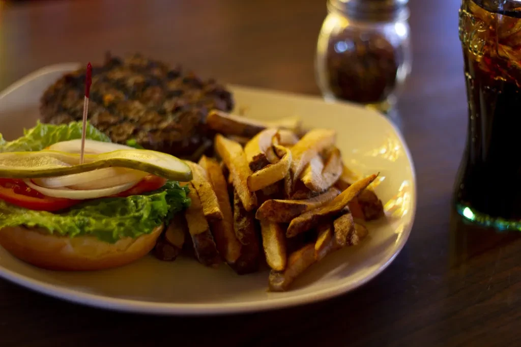 Deconstructed burger, golden fries, and cola on a dark wooden table.