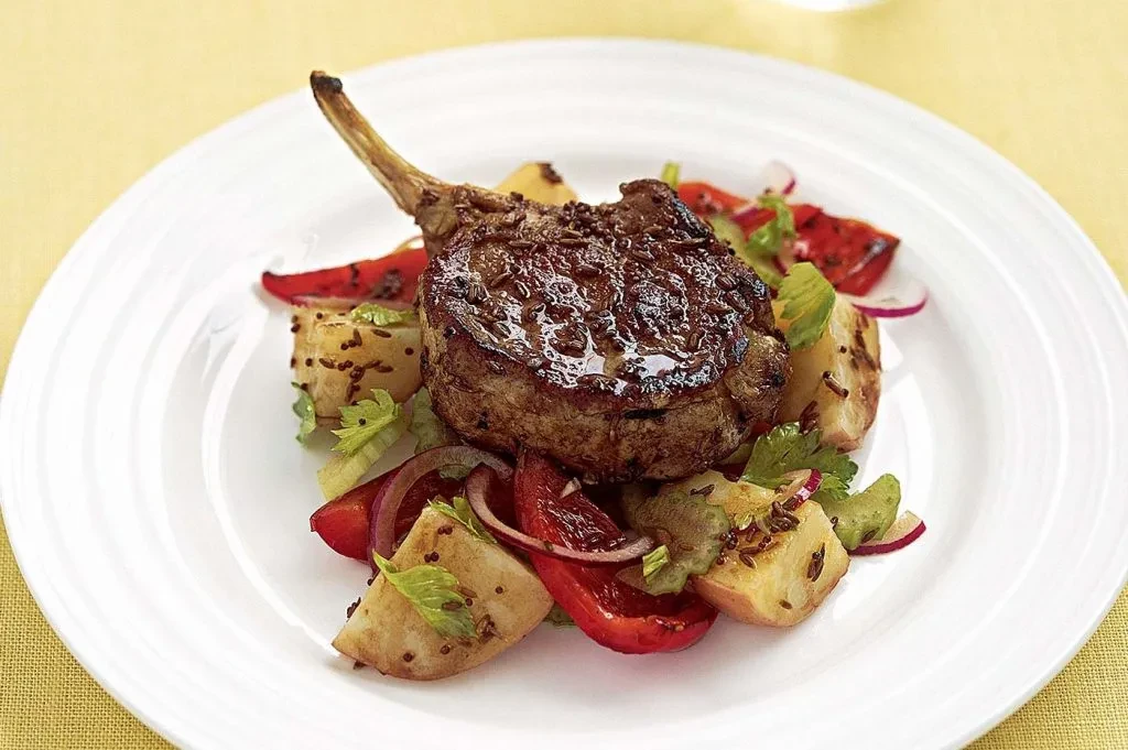 Seared lamb chop with bone, roasted vegetables, and spices on plate.