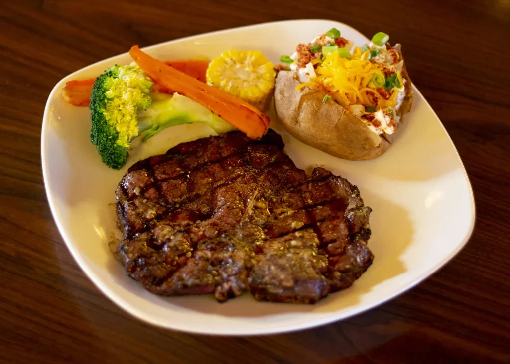 Grilled steak, loaded baked potato, corn, and mixed vegetables.
