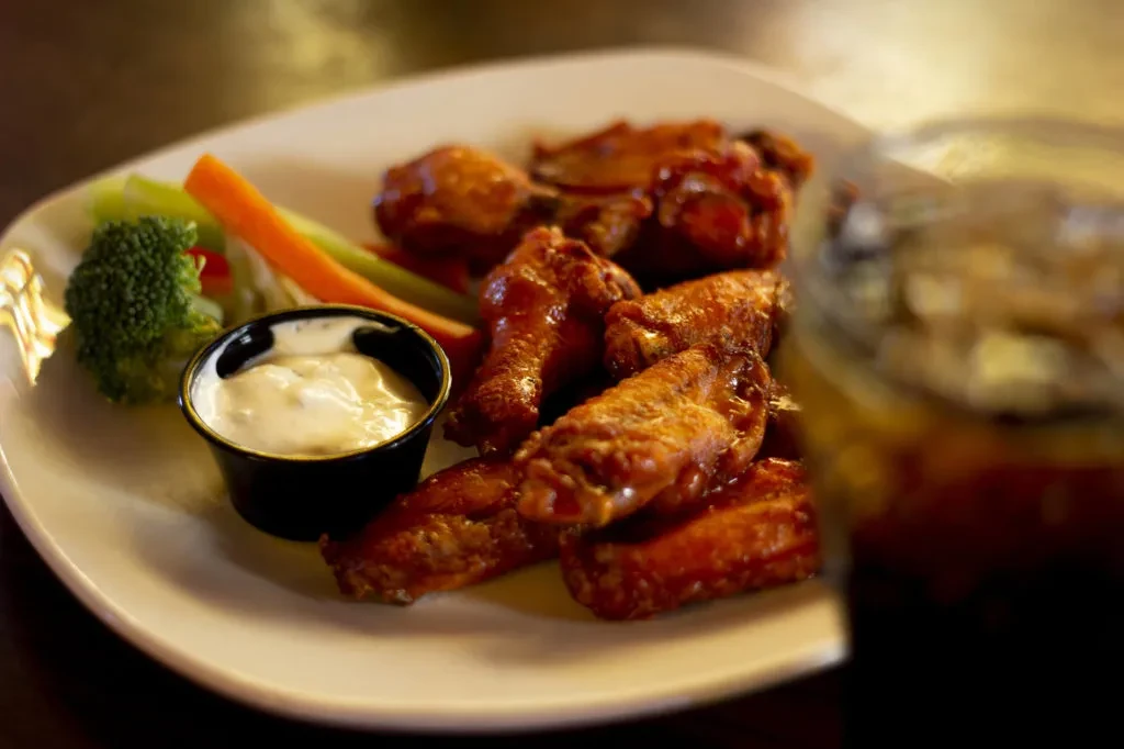 Plate of crispy chicken wings with dip and vegetable sticks.