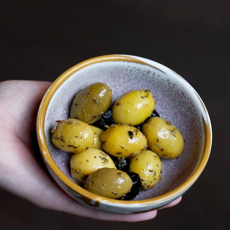 Rustic bowl of green, yellow, and black olives with herbs.