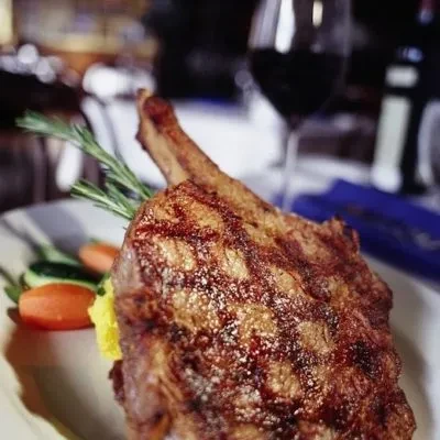 Grilled bone-in chop, rosemary, vegetables, and yellow purée on a plate.