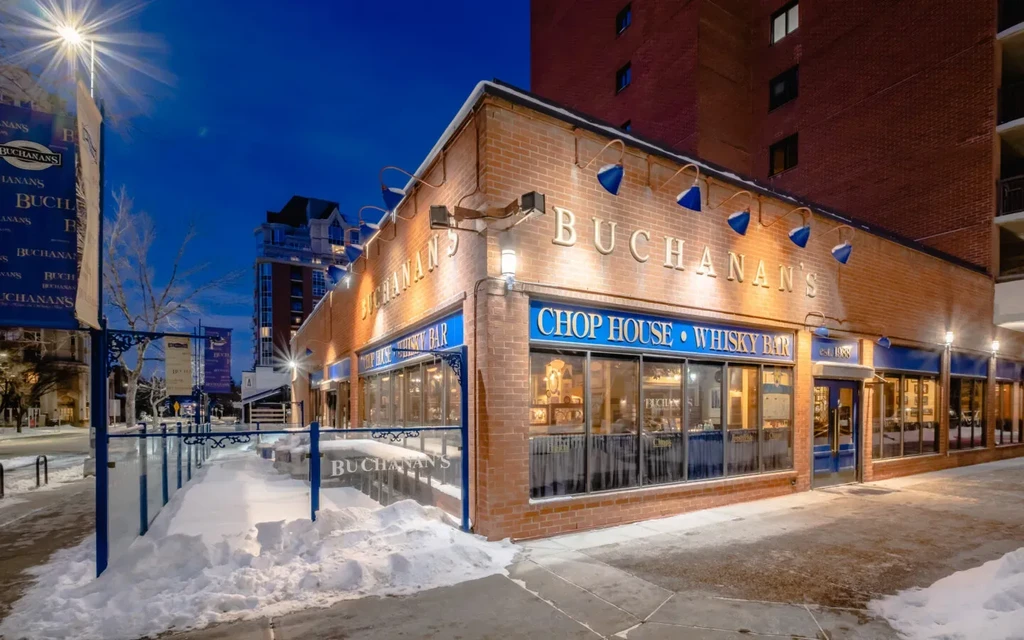 Illuminated brick exterior of Buchanan's Chop House & Whisky Bar, snowy.