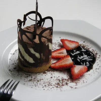 Cylindrical layered chocolate dessert with chocolate cage, strawberries, and compote.