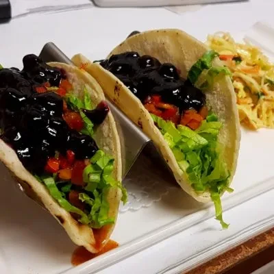 Two tacos with lettuce, vegetables, and dark berry sauce, plus coleslaw.