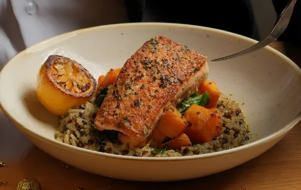 Seasoned salmon fillet with grains, roasted vegetables, and a charred lemon.