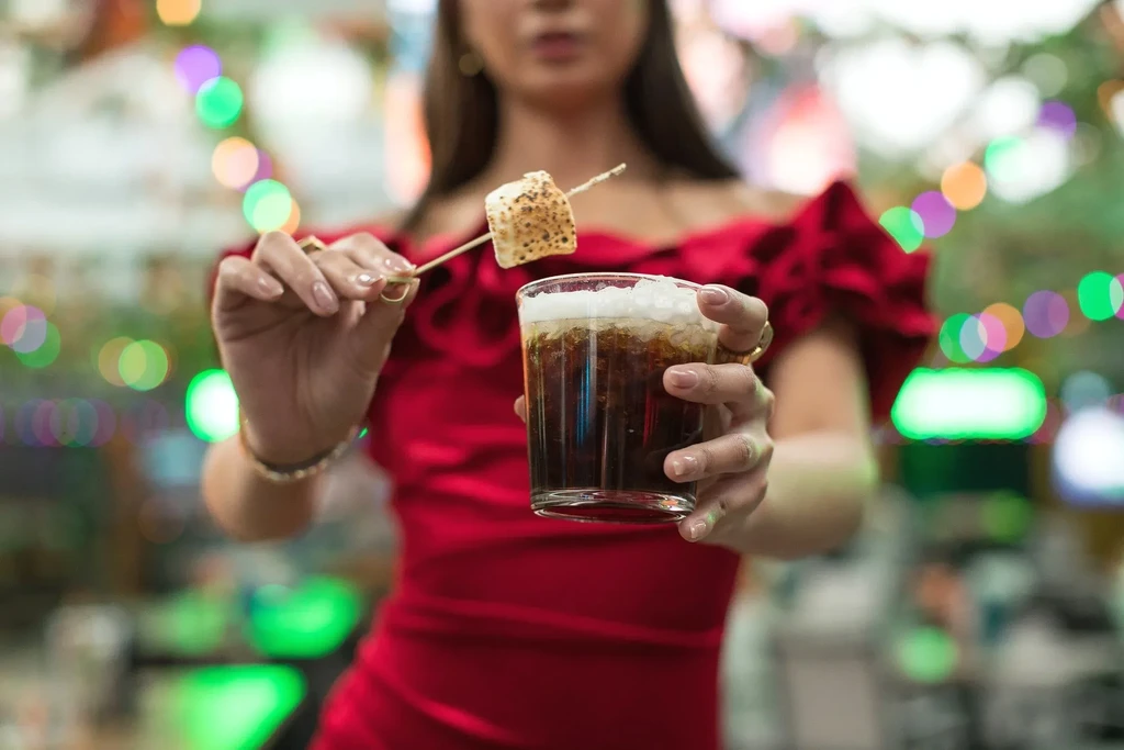 Close-up: Elegant hands hold a dark foamy drink and toasted marshmallow.