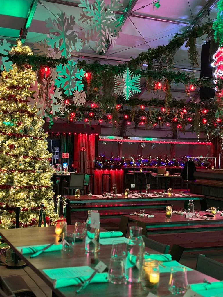 Festive restaurant interior with Christmas tree, garlands, and red and green lighting.