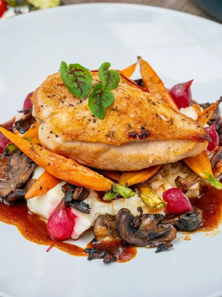 Plated seared chicken, creamy base, roasted carrots, mushrooms, radishes.