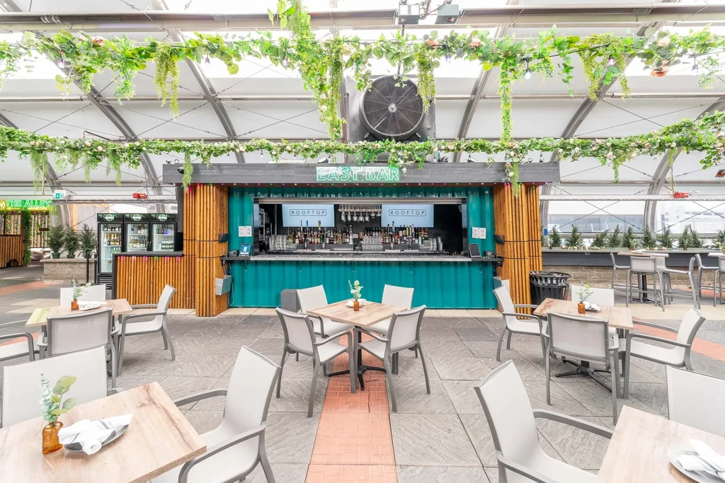 Rooftop bar, teal shipping container, "EAST BAR" neon sign.