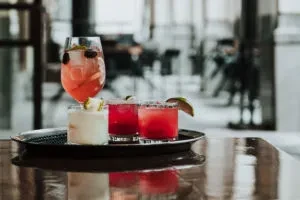 Assorted cocktails and a dessert on a reflective tray, blurred city view.